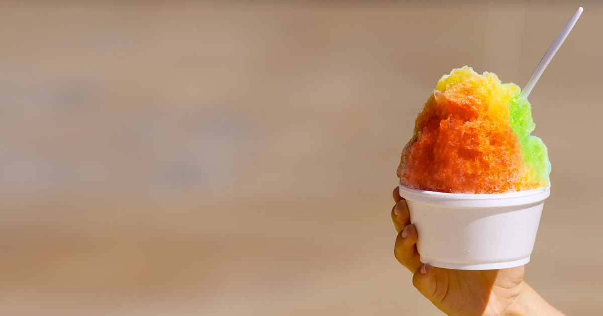 Hand holds colorful treat of shaved ice in front of blurred background