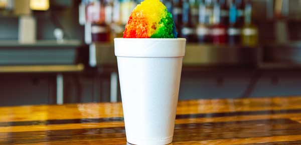 rainbow shave ice in white Styrofoam cup sitting on wooden tabletop