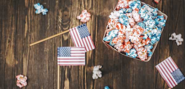 popcorn colored red and blue sitting in a box on a wooden table with small American flags