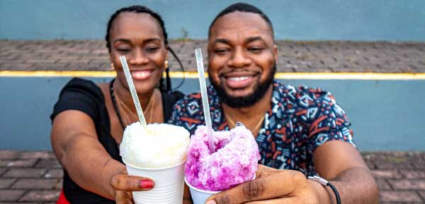 two adults sitting on street eating shave ice